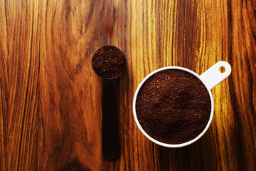 Taza medidora con café molido sobre una mesa de madera. Cuchara con café molido, vista superior.