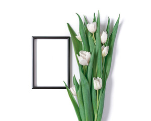 A bouquet of white tulips and a black blank photo frame are on a white background. Floral template with copy space from a bunch of fresh tulips. Flat lay, top view.