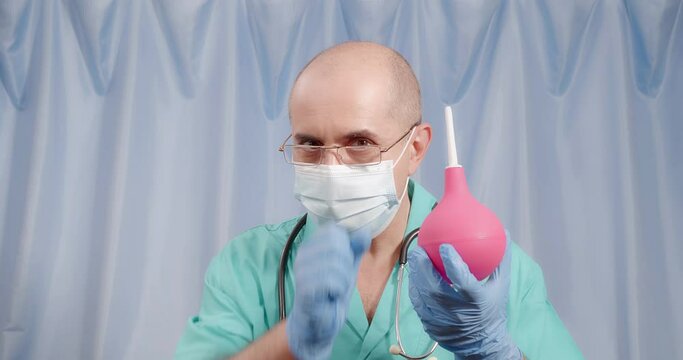 The doctor holds an enema in his hands. Pink pear syringe.