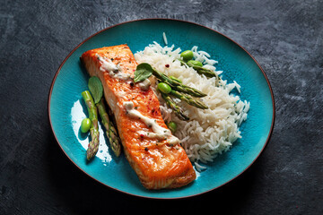Baked salmon with rice and asparagus on gray background.