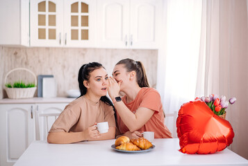 A happy female couple is celebrating Valentine's Day at home. two beautiful young girls are sitting...