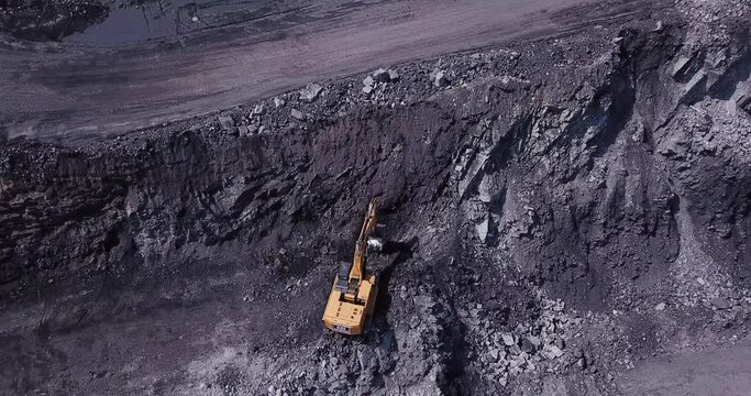 Aerial view of process of mining coal in a quarry. Drone flying above yellow dump trucks and mine excavators at coal mining area.