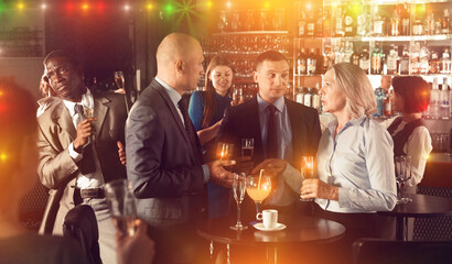 Group of executives holding glasses with alcohol drinks and talking at office party