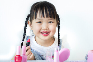 A cute Asian girl is enjoying her makeup with makeup on the table. The back has a white background.