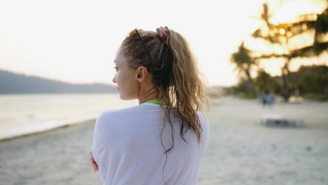 Close up portrait woman in a white tunic shirt on beach, near stormy sea. Girl in sunglasses. Female tourist walks