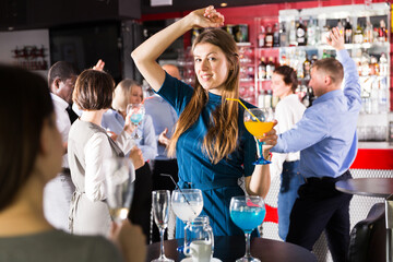 Cheerful attractive girl with cocktails having fun with workmates on corporate party at nightclub
