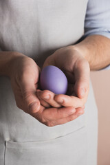 Man hands hold easter egg painted in purple color. Preparing for Easter, cooking in home kitchen. Close up, vertical