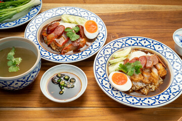 Rice with red roasted pork, Crispy Pork with sauce and Egg topped in a white dish on wooden table.