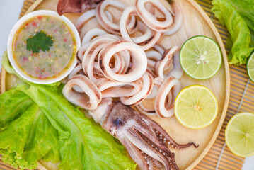 Fototapeta na wymiar squid rings on wooden plate, Fresh squid cooked boiled with lettuce vegetable salad lemon and seafood sauce on table background