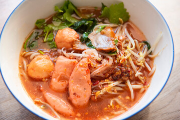 Red soup noodle pork with red roasted pork and bean sprout vegetable in soup bowl on wooden table, top view Thai and China Asian food