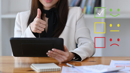 Young businesswoman using digital tablet for selecting smiley face icon to evaluate product and...