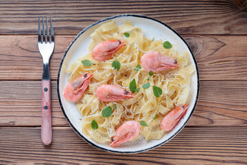 Top view of pasta fettuccine with shrimp in rustic plate with fork on wooden background.