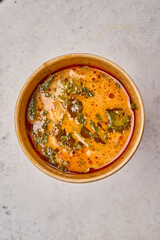 Macro view Tom Yam soup with salmon and seafood in a paper solid container on light background. Vertical orientation