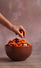dried apple slices in a brown dish with a hand on a pink background