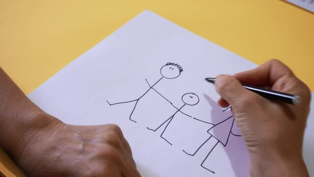 Crop View Of Person Drawing Stick Figures Of A Family On White Bond Paper. High Angle