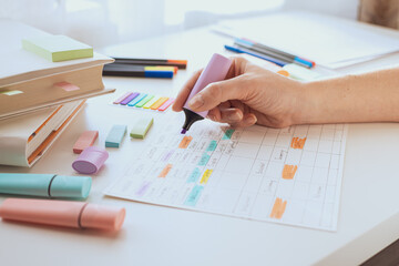 A woman's hand draws with a marker or purple text highlighter on a sheet with a schedule. Student...