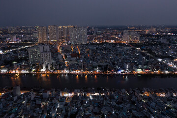 Panoramic view drone shot of Ho Chi Minh City in late evening looking across the Kenh Te canal with reflections and illuminated buildings.