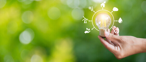 Close up image of hand holding a light bulb on green background with save energy icon showing the...
