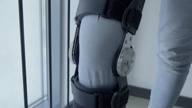 Close-up of Knee in Metal Skeleton. Tendon Injury. Postoperative Recovery. Exoskeleton. Girl Gently Bends Injured Knee. Bandage. Orthopedics. Fragility of the Human Body. Trains to Walk. Metal Mounts