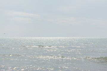 Obraz premium Grey sea background top view. The texture of a serene calm ocean with a passing seagull above it. The concept of peace, relaxation, solitude. Bright sun glare on the water. Natural neutral background