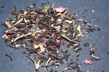 Dry tea with green leaves in wooden spoons, on black background.