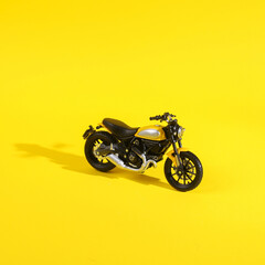 Obraz na płótnie Canvas Toy motorcycle on a yellow background with a shadow. Minimal layout