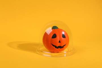 Halloween pumpkin jack under transparent dome on yellow background. Protection, isolation concept. Minimal layout