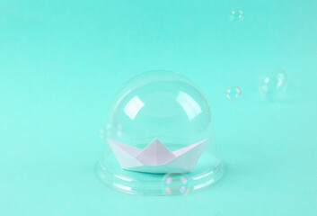 Paper sailboat under transparent dome with bubble on blue background. Protection, isolation concept. Minimal layout