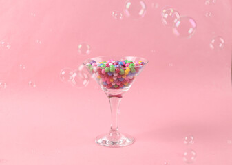 cocktail glass with colored balls and soap bubbles on pink background