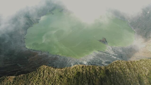 Aerial backward movement shot of white clouds blowing across the crater and lake of El Chichonal volcano in Chiapas, Mexico on a cloudy day
