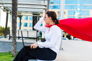 unhappy tired business woman with a superhero cape is sitting with a laptop