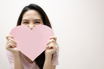 Asian beautiful woman  are holding Pink heart shape paper  covering her mouth  with smile and happiness.A Valentine day and Love.