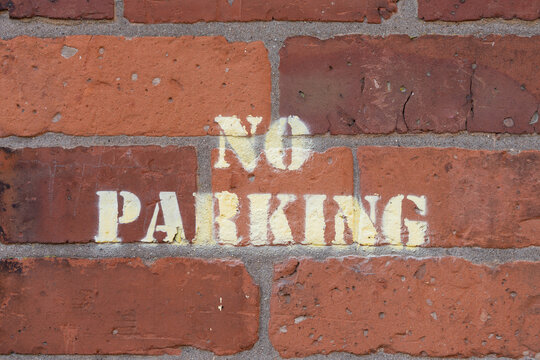 No car parking sign sprayed on red brick wall with yellow paint to denote parking prohibition.