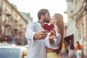Young couple in love hold a red heart, show their love and kiss in the city. Romantic concept