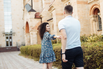 Fototapeta na wymiar Follow me. Young woman pulls a young guy along while walking against the background of old european architecture