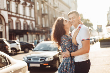 Fototapeta premium Cute curly girl kissing her boyfriend on the cheek in the city