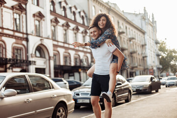 Fototapeta na wymiar Couple in love. Man carrying girl on his back in the street. Smiling man with beautiful young woman, ride piggyback, having fun together. Relationship concept.