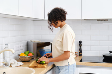 Young african american housewife cuts cucumber for salad
