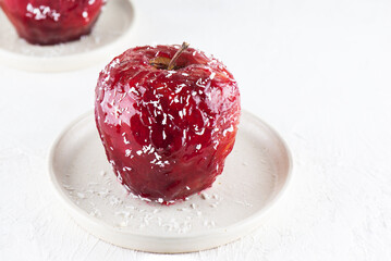 Baked apple with walnuts and honey in red glaze with coconut flakes on a table.