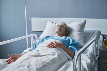 Senior woman lying on the bed at hospital ward, she being treated at hospital