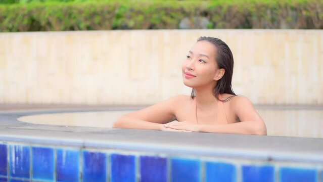 Attractive asian woman on edge of swimming pool looking around, slow motion