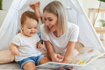 Happy woman mom and her little daughter read book in wigwam at home