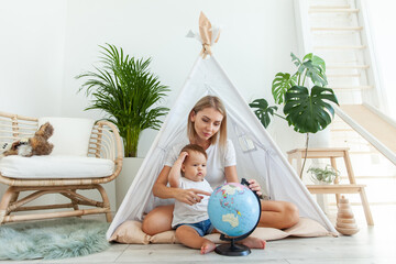 Mom with a little daughter sitting in a wigwam at home, studying the globe. Spend time together. Matyrdom concept © splitov27