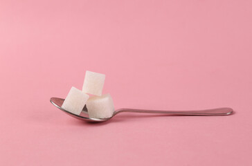 Spoon with sugar cubes on pink background