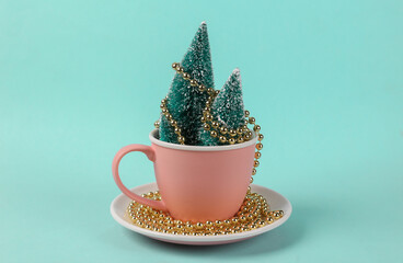 Ceramic cup with mini Christmas tree .and garland on blue background. Minimal christmas still life