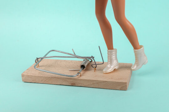 Minimal layout. Doll feet stepped into a mousetrap on a blue background. Deception, trap