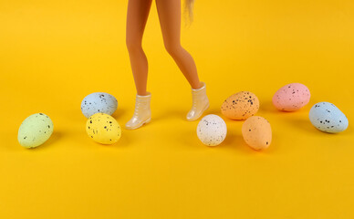 Easter minimal concept. Feet of girl doll in boots with colorful easter eggs on yellow background