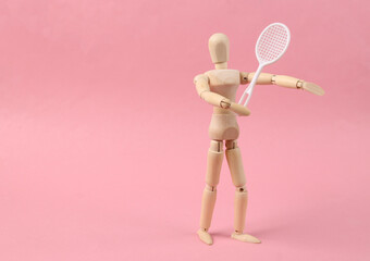 Wooden puppet with tennis racket on pink background