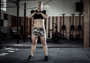 Naklejka na ściany i meble Muscular woman athlete holding heavy kettlebells. Functional, cross training in a modern gym.