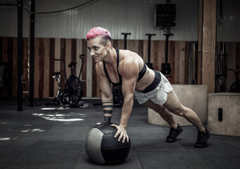 Muscular athletic woman push ups with medicine balls in a modern gym. Cross fit, functional training